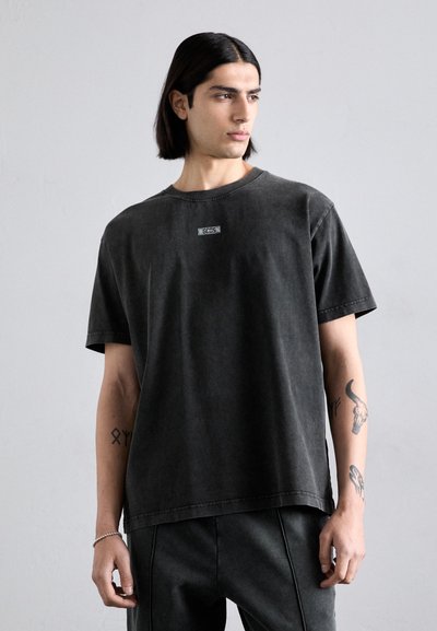 T-shirt en coton noir avec un col rond et des manches courtes, comportant une petite étiquette logo à l'avant et une coupe décontractée.