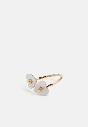 Bague ajustable en ton doré mettant en avant deux accents en forme de cœur blancs avec des motifs en relief et des détails en étoile au centre, embellie de petits gemmes.
