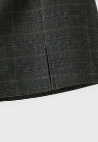 Gros plan d'un tissu gris foncé avec un motif à carreaux subtil et une petite fente verticale près du bord inférieur.