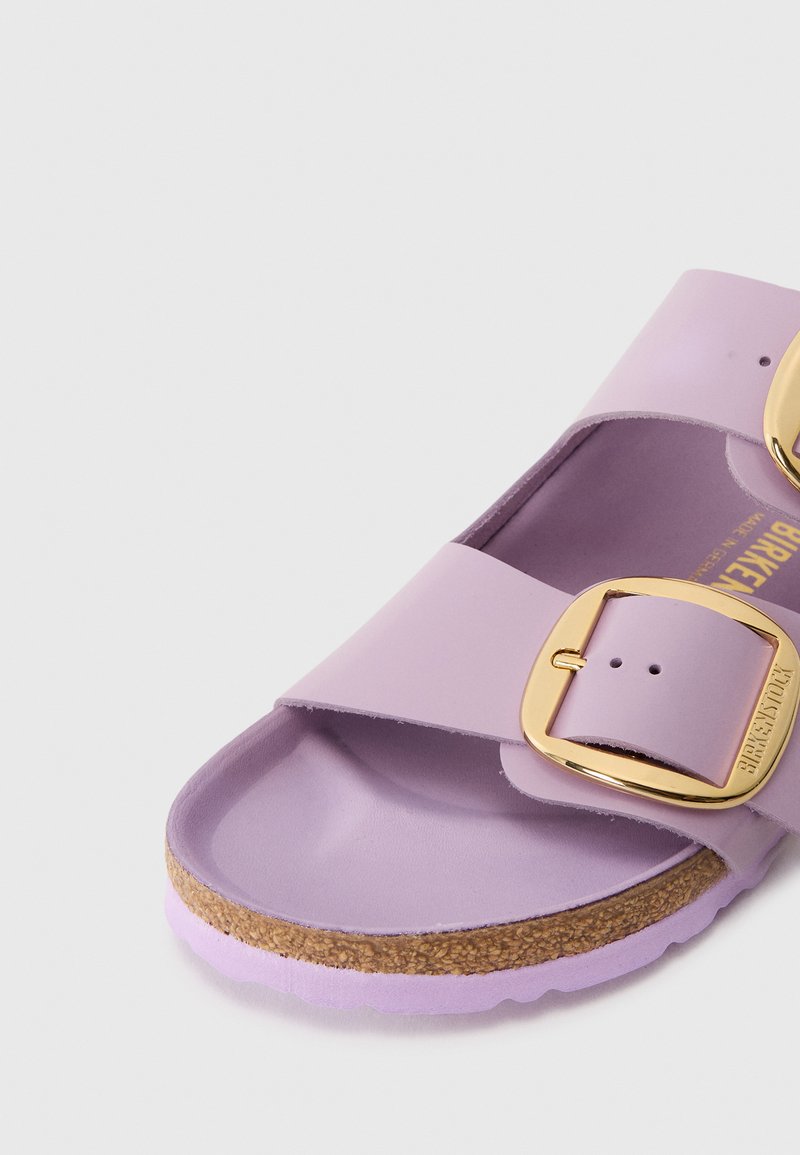 Lila Rutschen-Sandel mit zwei breiten Riemen, goldenen Schnallen, Korkfußbett und strukturierter lilafarbener Sohle auf weißem Hintergrund.