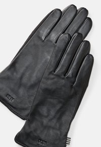 Black leather gloves with a smooth texture, fitted design, and five fingers. Branding "MN" embossed on the wrist.