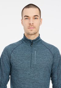 Maglione zip-up manica lunga di colore blu scuro, realizzato in tessuto testurizzato e traspirante, con collo alto e dettagli cuciti sulle spalle.
