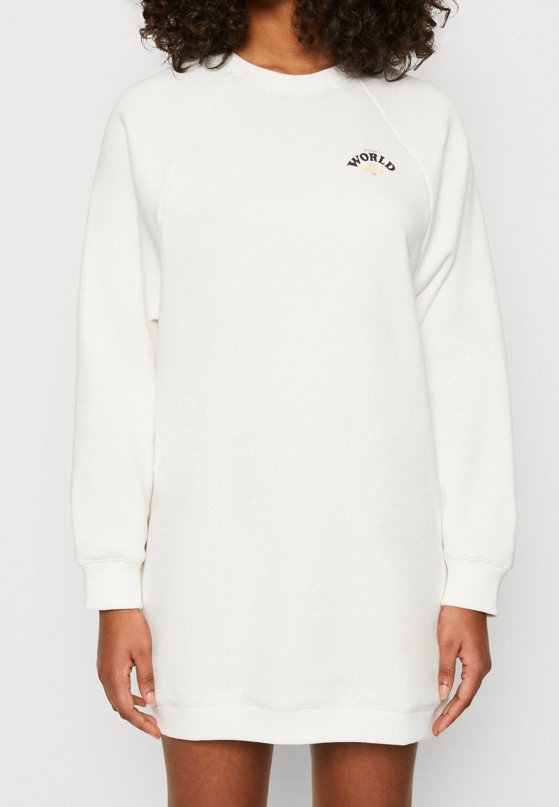Vestido sudadera blanco con mangas raglán, puños y dobladillo acanalados. Presenta un pequeño gráfico de "WORLD" en negro y rojo en la parte superior del pecho. Textura suave.