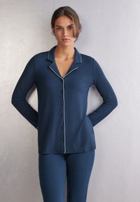 Mörkblå långärmad pyjamasuppsättning med vitt piping, med knapplist framtill och krage. Mjuk, slät tyg.