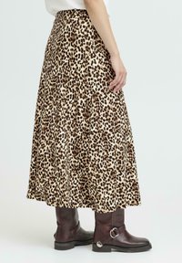 Maxi kjol med leopardmönster i beige och brunt, gjord av tyg med en veckad design. Bärs med bruna knähöga stövlar med spännvidd.
