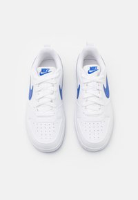 White Nike sneakers featuring blue accents and perforated details, with flat laces and a textured rubber sole.