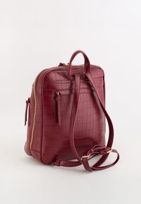 Czerwony plecak ze skóry tłoczonej w wzór krokodyla, o prostokątnym kształcie, z dwoma paskami, górnym uchwytem i złotymi elementami ozdobnymi.