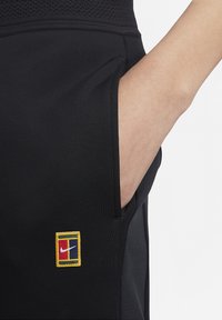 Svarta träningsbyxor med en sidoficka, med en rektangulär flerfärgad Nike-logotypapplikation. Materialet ser slätt ut med en figurnära design.