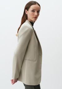 Hellbeige maßgeschneiderte Blazer mit einer strukturierten Passform, einem Einzelknopfverschluss und zwei Seitentaschen. Glatte Textur, scharfe Revers und minimales Design.