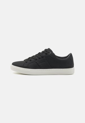 Sneaker sintetiche nere con una superficie liscia, caratterizzate da cuciture minime, suola in gomma bianca e allacciatura frontale. Logo in rilievo sul lato.