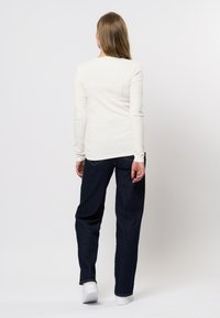 Witte ribbeltrui met lange mouwen en een aansluitende pasvorm, gecombineerd met donkerblauwe rechttoe-rechtaan jeans en witte sneakers.