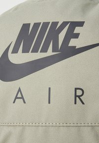 Ljusgrön texturerad tyg med en framträdande svart Nike-logotyp och "AIR"-bokstäver under. Sömmar synliga längs den nedre kanten.