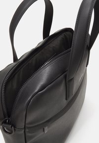 Schwarze Handtasche mit glatter, strukturierter Außenseite und zwei Griffen. Verfügt über einen Reißverschluss oben und ein geräumiges, gefüttertes Innenfach.