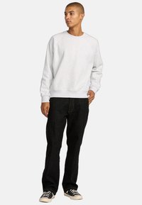 Grijze sweatshirt met een ronde hals, geribbelde manchetten en zoom, gecombineerd met zwarte rechttoe rechtaan spijkerbroek en zwarte sneakers, staand tegen een neutrale achtergrond.