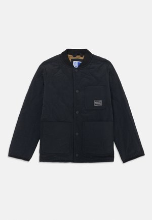 Svart vadderad jacka med rund krage, tryckknappar, två framfickor och en etikett på bröstet. Har en slät yta och minimalistisk design.