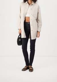 Beige oversized button-down jacket, white crop top, dark skinny jeans, black handbag, and leopard print flats with straps.