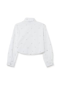 Camisa blanca corta con mangas largas, un collar puntiagudo y un sutil patrón gris bordado de corazones. Textura de tela suave.