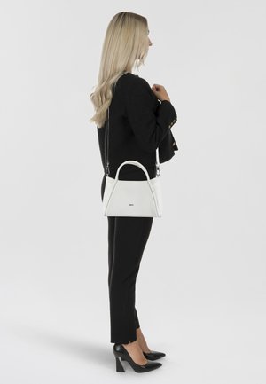 Borsa a tracolla in pelle bianca con una silhouette curva, dotata di doppio manico superiore e una tracolla rimovibile, esposta accanto a una persona in abbigliamento nero.