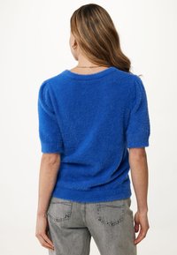 Niebieski puszysty sweter dzianinowy z krótkimi rękawami, okrągłym dekoltem i luźnym krojem, w połączeniu z jasnoszarymi spodniami typu high-waisted.