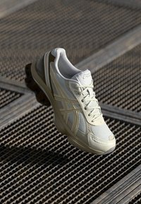White athletic shoe with mesh upper, yellow accents, and textured sole. Features lace-up closure and brand logo on the side.