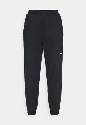 Sorte fleece joggers med elastisk liv, avsmalnende ben, sidelommer, og en liten hvit logo på venstre ben.