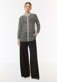 Black and white patterned long-sleeve blouse with a collar, button-up front, and contrasting cuffs. Paired with wide-legged black trousers.