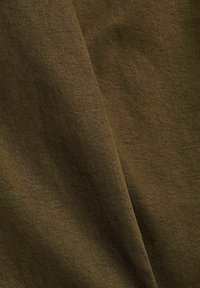 Gros plan d’un tissu marron montrant une fine texture tissée et un pli diagonal créant ombre et profondeur.