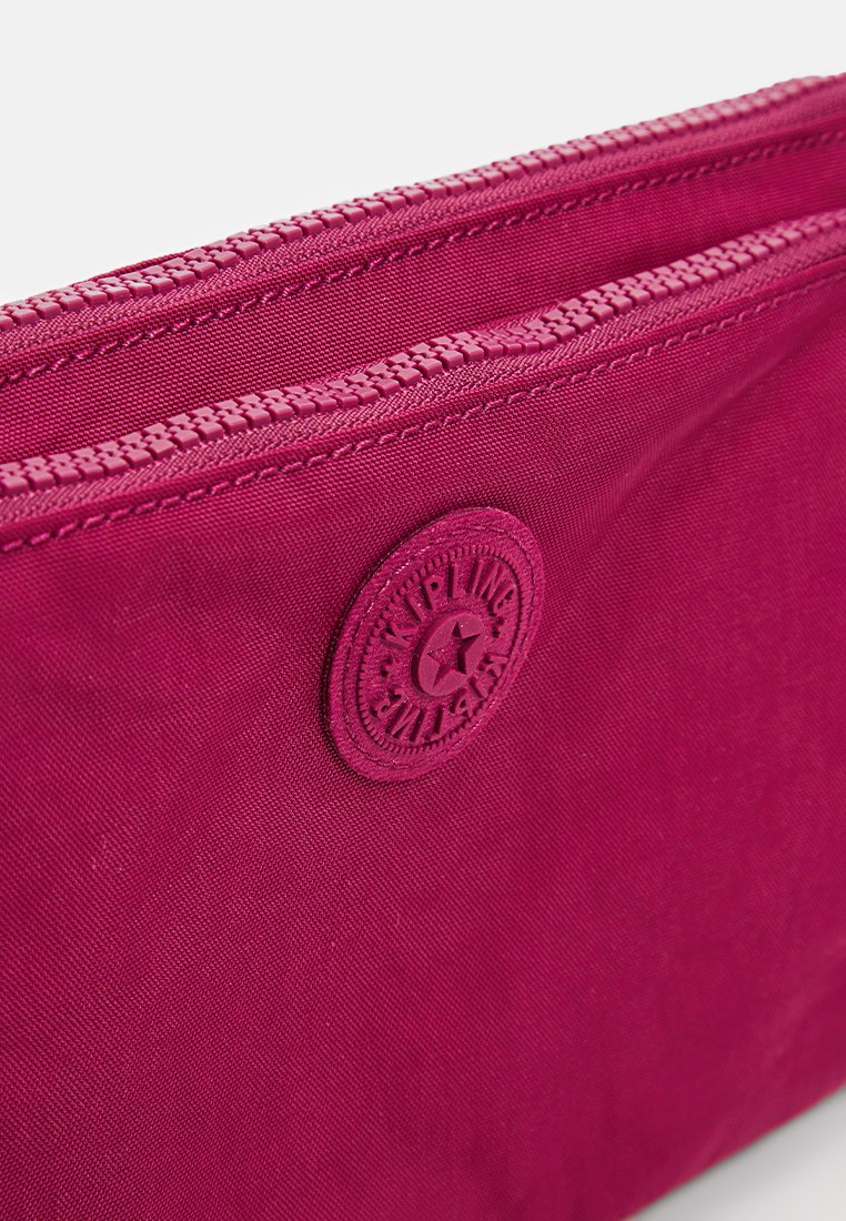 Pochette di tessuto magenta con due cerniere visibili e un'etichetta rotonda del marchio Kipling cucita sul davanti.