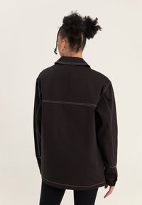 Giacca nera oversize con colletto, cuciture bianche e taglio dritto. Presenta maniche lunghe e una texture del tessuto liscia.