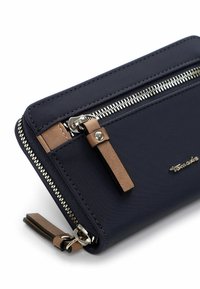 Navy fabric wallet with silver zipper, brown leather accents, and logo detail. Features a zippered compartment and rectangular shape.