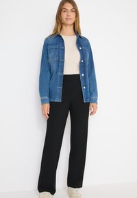 Jeansjacka i medelblått, med två bröstfickor och silverfärgade knappar. Matchad med högmidjade svarta byxor och ljusa sneakers.
