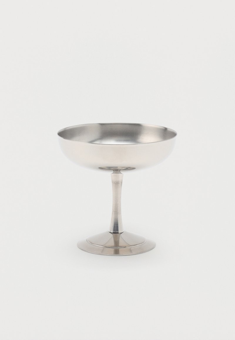 Srebrn kovinski kozarec za sladice ali šampanjec s široko, plitvo skodelico in močnim steblom na ravni podstavi.