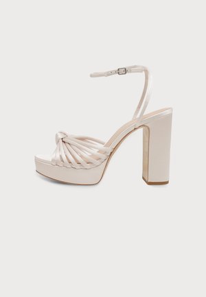 Sandale à plateforme couleur crème, avec une pointe composée de plusieurs brides nouées, une bride de cheville à boucle et un talon haut et carré, vue de profil.