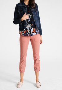 Veste en denim, blouse fleurie et pantalon court pêche avec poignets élastiques. Des ballerines douces ornées de nœuds complètent la tenue.