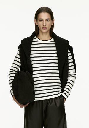 Black sleeveless wool vest over a white shirt with black stripes, paired with sleek black leather pants and a black suede bag.