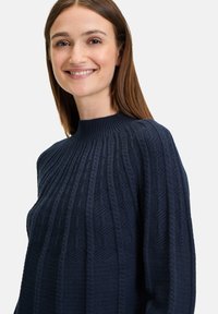 Granatowy sweter dzianinowy z wysokim dekoltem, fakturowanym ściągaczem oraz geometrycznymi wzorami z przodu i na rękawach.