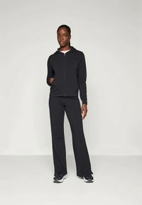 Melna zip-up kapuce ar priekšējo kabatu, saskaņota ar melniem platiem biksēm. Apģērbs izceļas ar vienkāršu dizainu un gludu auduma tekstūru.