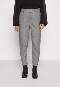 Pantalons à carreaux gris avec une coupe ajustée, présentant une taille haute et des plis subtils, associés à des bottines noires.