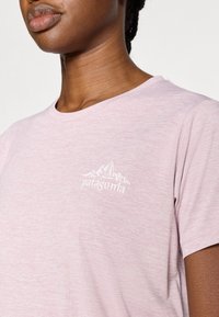 Ανοιχτό ροζ κοντομάνικο T-shirt από μαλακό ύφασμα, με λευκό λογότυπο Patagonia και γραφικό βουνού στο πάνω αριστερό μέρος το υ στήθους.