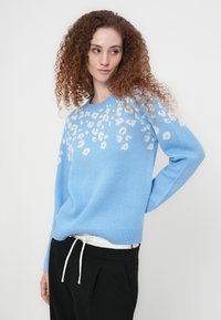 Ανοιχτό μπλε πουλόβερ με λευκές λεοπάρ κηλίδες, στρογγυλή λαιμόκοψη, μακριά μανίκια και άνετη εφαρμογή, σε συνδυασμό με μαύρο παντελόνι.