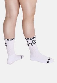 Valkoiset puuvillasukat, joissa ruudullinen kuvio yläosassa ja mustia kilpatähtiä. Resorikuviointi ja jalassa kontrastivärinen musta raita.