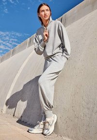 Grijze sweatshirt en bijpassende joggers van zachte stof, met een hoge kraag en elastische manchetten, gecombineerd met beige sneakers.