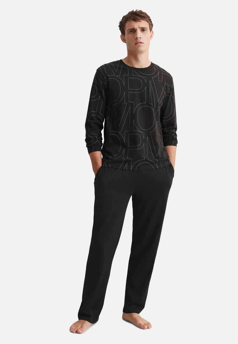 Haut noir à manches longues avec un motif de texte grand contraste, associé à un pantalon noir. Tissu doux, coupe décontractée, jambes droites, et sans accessoires visibles.
