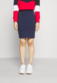 Marinblå åtsittande kjol kombinerad med en färgblockerad tröja i röd, vit och svart. Bärs med vita sneakers som har en slät yta.