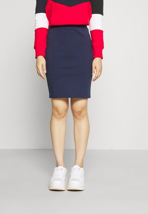 Marinblå åtsittande kjol kombinerad med en färgblockerad tröja i röd, vit och svart. Bärs med vita sneakers som har en slät yta.