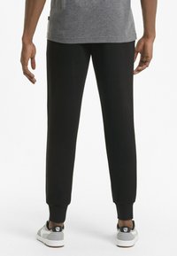 Sorte joggerbukser med ribbede manchetter, der har en glat tekstur og elastisk talje. Båret med hvide og grå sneakers.