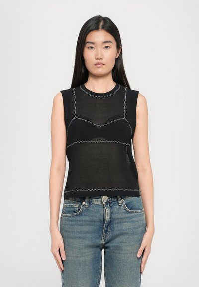 Top sans manches noir avec une texture en mesh, présentant une couture blanche contrastante et un design ajusté. Associé à un jean en denim bleu.