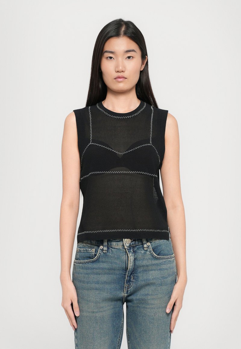 Top sans manches noir avec une texture en mesh, présentant une couture blanche contrastante et un design ajusté. Associé à un jean en denim bleu.