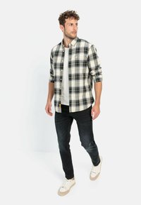 Herrenhemden mit Karomuster in Schwarz, Weiß und Gelb; Knopfdesign mit hochgekrempelten Ärmeln. Kombiniert mit dunklen Jeans und hellen Sneakers.
