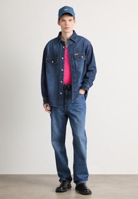 Τζιν πουκάμισο και τζιν σε μπλε, συνδυασμένα με ροζ τοπ και μπλε καπέλο. Μαύρα παπούτσια ολοκληρώνουν την εμφάνιση. Δύο εμπρόσθιες τσέπες στο πουκάμισο.